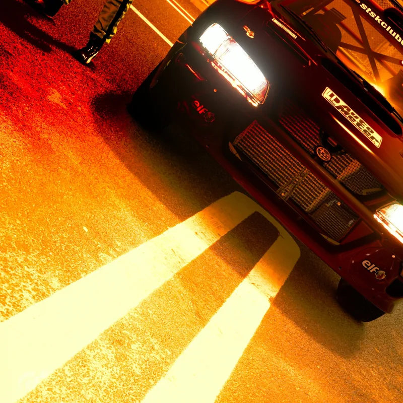 A dark car with headlights on in the Shinkura parking area, Gran Turismo 7.